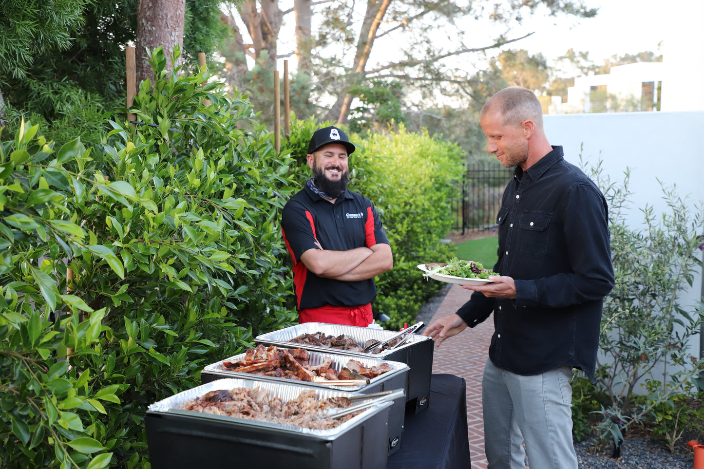 Worker smiles as a catering customer chooses from Corbin's Q pulled pork, pork ribs, or tri tip.