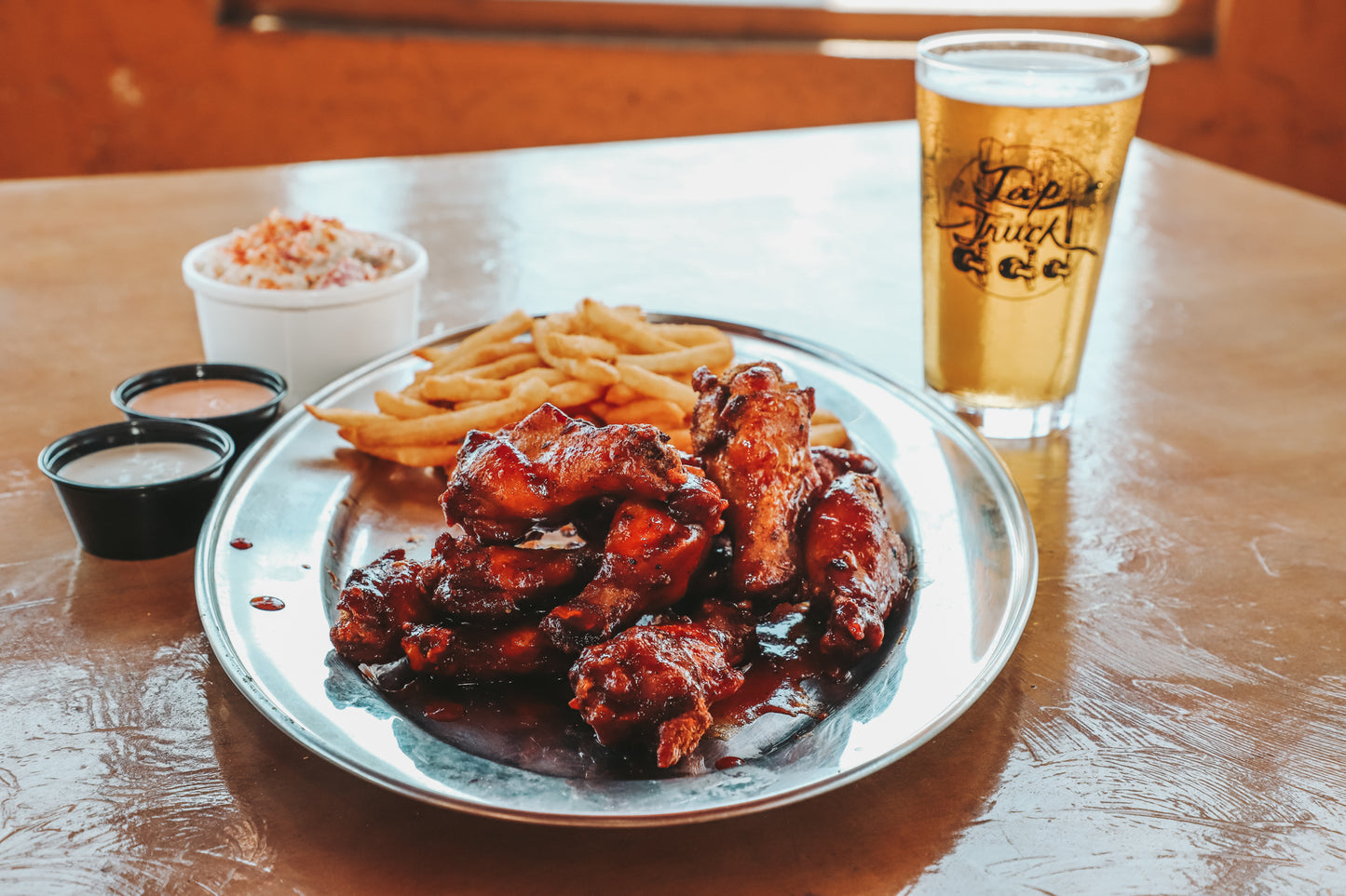 A platter of a dozen saucy barbecue wings with a side of fries, coleslaw and a cold beer to wash it down. 