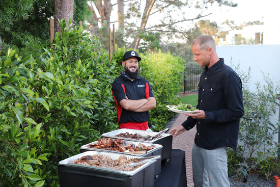 Worker smiles as a catering customer chooses from Corbin's Q pulled pork, pork ribs, or tri tip. 