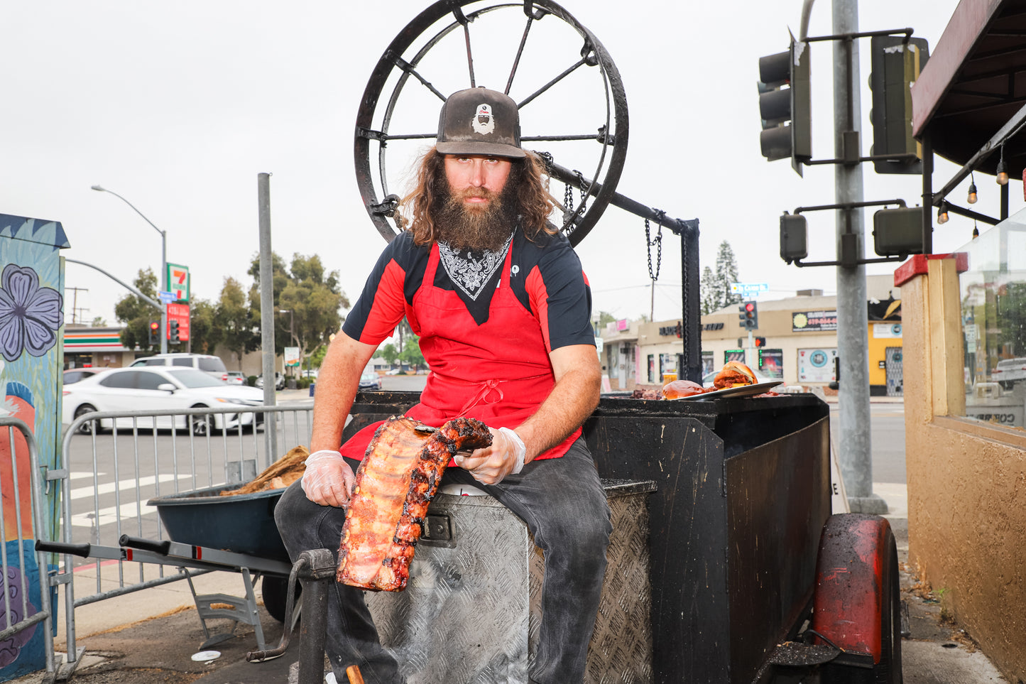 Corbin sitting on his Santa Maria style grill holding a full rack of pork ribs. 