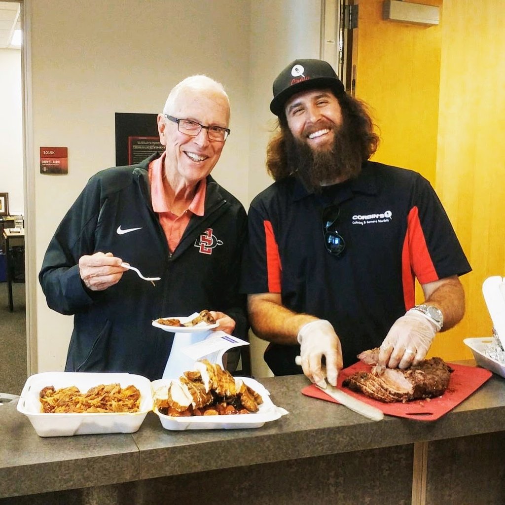 Corbin slices up some delicious tri tip while the guest of a catering event stands next to him smiling and enjoying his meal. 