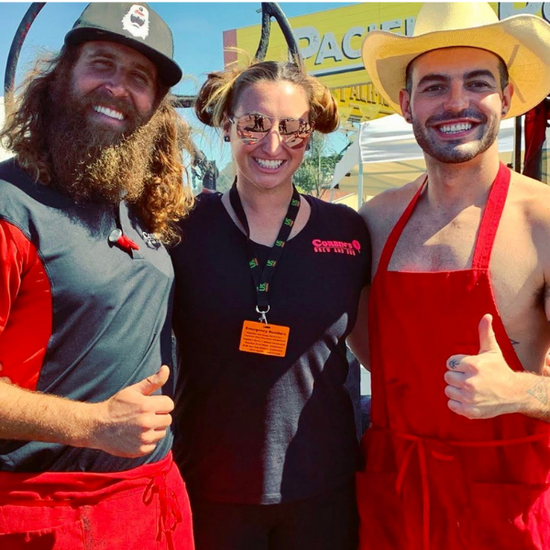 Corbin, his wife Meghan, and a friend hold a thumbs up while serving barbecue at a farmers market in San Diego. 