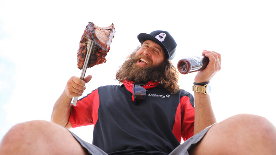 Corbin, owner of Corbin's Q Bar and Barbecue, smiling while holding up a rack of pork ribs and his sweet barbecue sauce. 