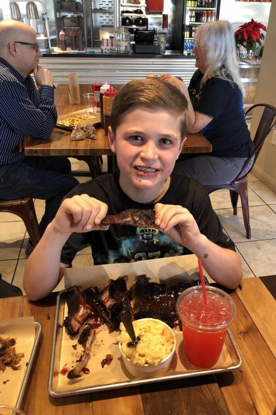 A kid smiles as he enjoys some saucy pork ribs from Corbin's Q bar and barbecue. 