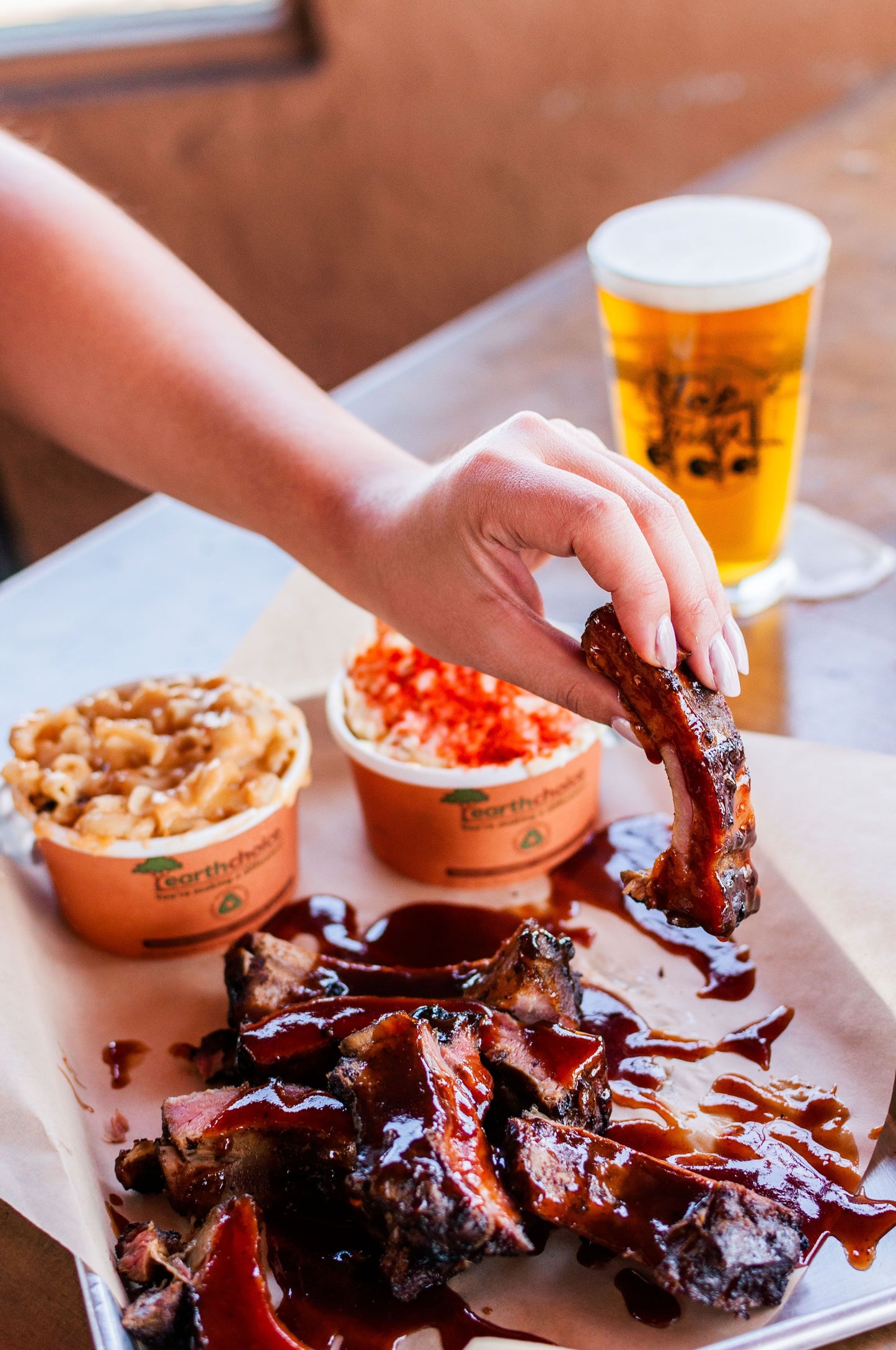 A customer picks up a saucy pork rib accompanied by mac n cheese, potato salad, and a cold beer. 