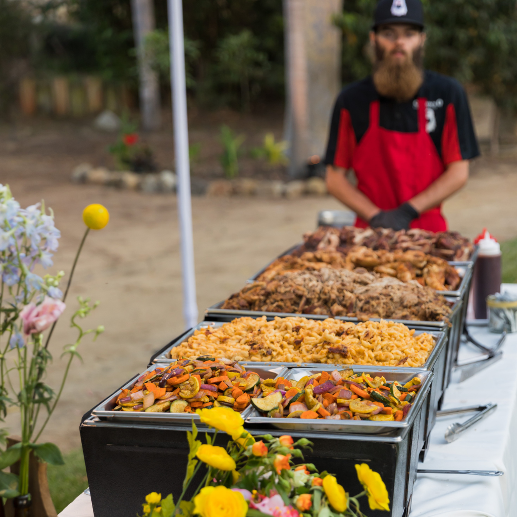 A buffet style meal is ready to be served to the guests of an on-site catering event. They can choose from mac n cheese, grilled veggies, pulled pork, chicken, and tri tip all from Corbin's Q bar and barbecue. 